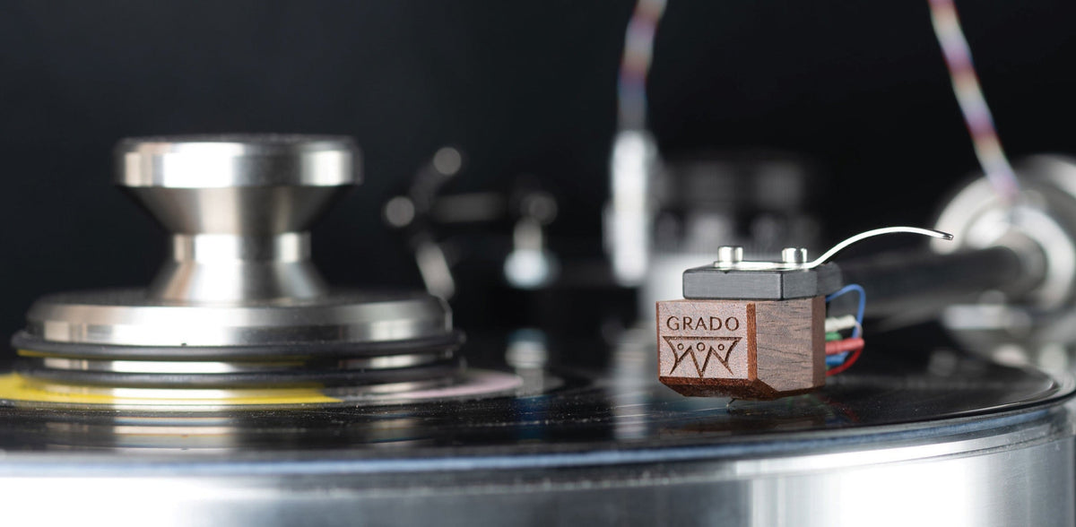 A Grado wood-body phono cartridge on a headshell, close up over a polished turntable platter, with the edge of a record and the spindle in frame