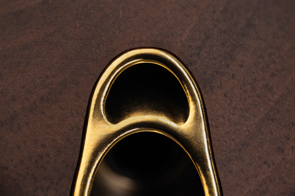 Extreme macro of the brass yoke fitting against the 99 Classics walnut cup. Brushed gold and brown grain, no product silhouette, shallow focus.