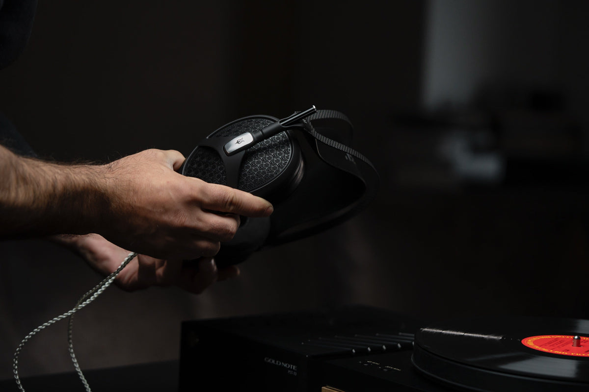 A man's hands lifting Empyrean II off a turntable plinth, an orange-labelled record spinning below, tonearm visible, very dark surround.