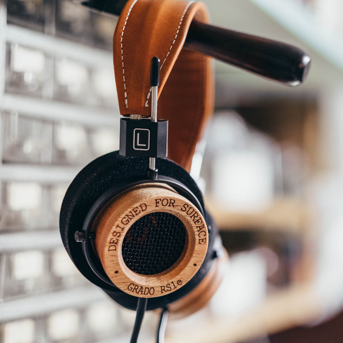 A Grado RS1e hanging by its tan leather headband from a dark rail, in front of a blurred wall of pale drawers