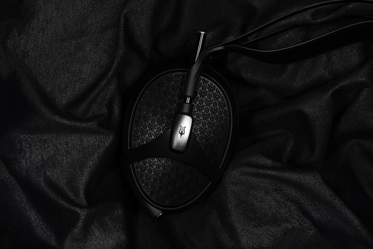 A Meze Empyrean II lying on crumpled black fabric, lit from one side, its cable running out of the frame