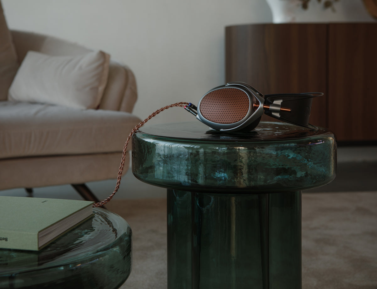 A Meze Poet folded on a green glass side table next to a book, a pale sofa and a coffee table behind it in daylight