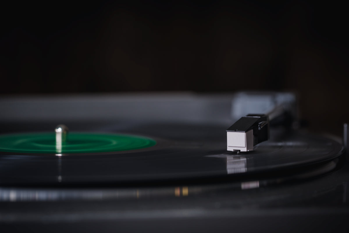 A turntable cartridge playing a black record with a green label, close up at platter level