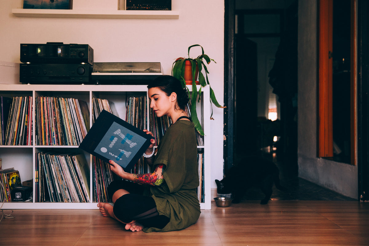 Someone sitting on the floor in front of a record collection, pulling a sleeve out to look at it