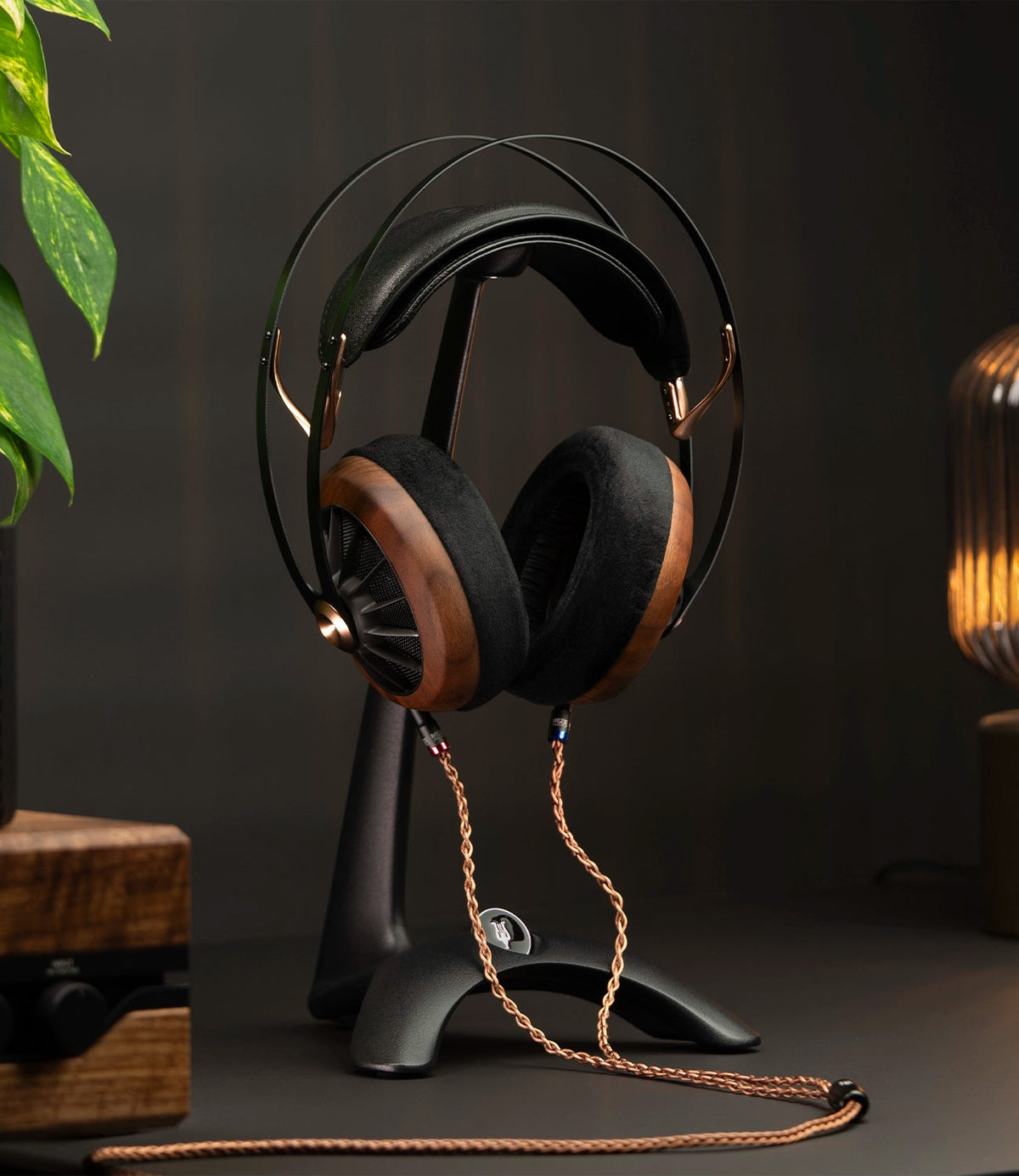 Meze Audio Manta Headphone Stand, holding a wood-cup Meze headphone on a desk beside a lamp