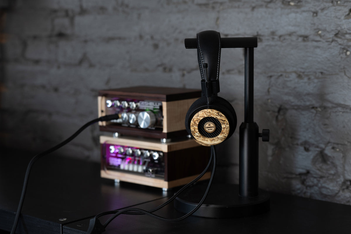 Grado Hemp hanging on a headphone stand beside a stacked amplifier, in front of a painted brick wall