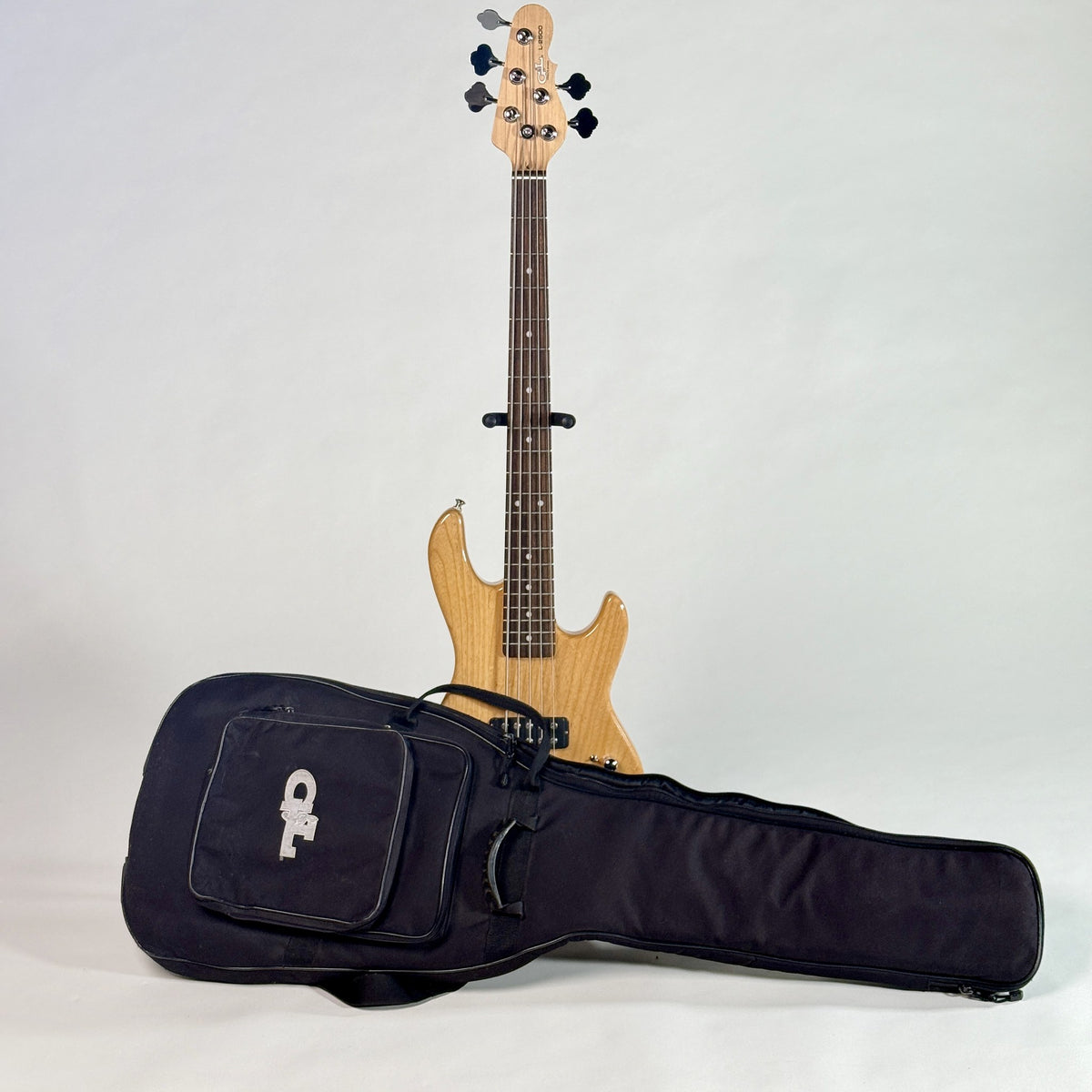 Used G&L Tribute L-2500 five-string bass, natural, standing behind its G&L gig bag