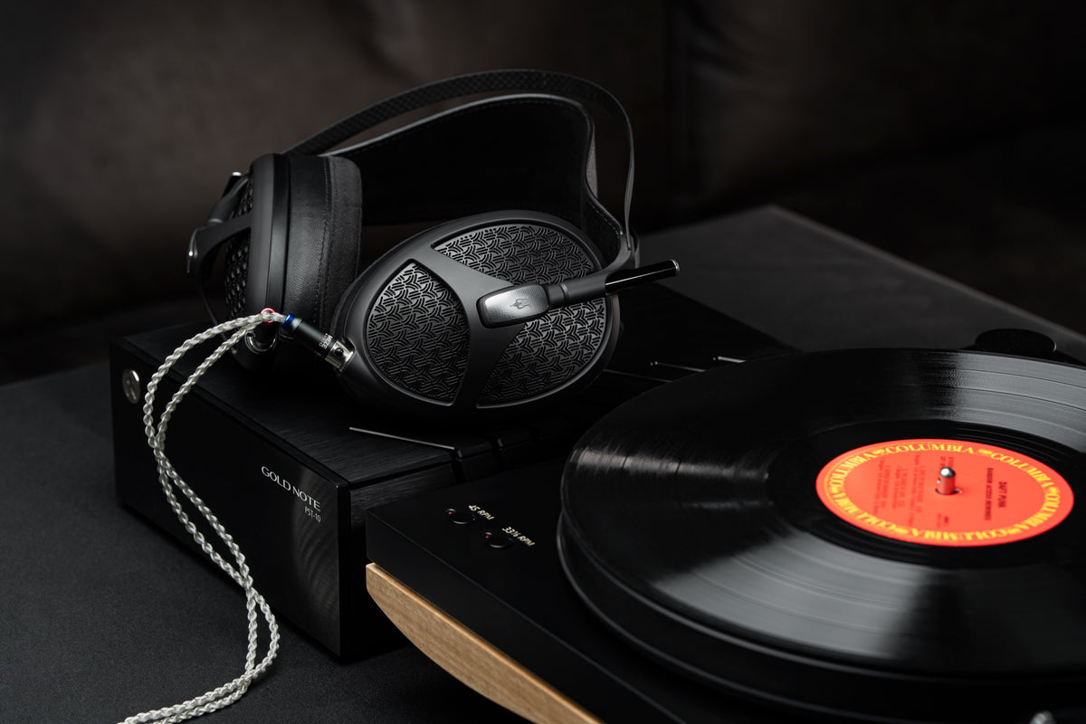 A Meze Empyrean II resting on a turntable beside a spinning record with an orange label, its silver cable across the plinth