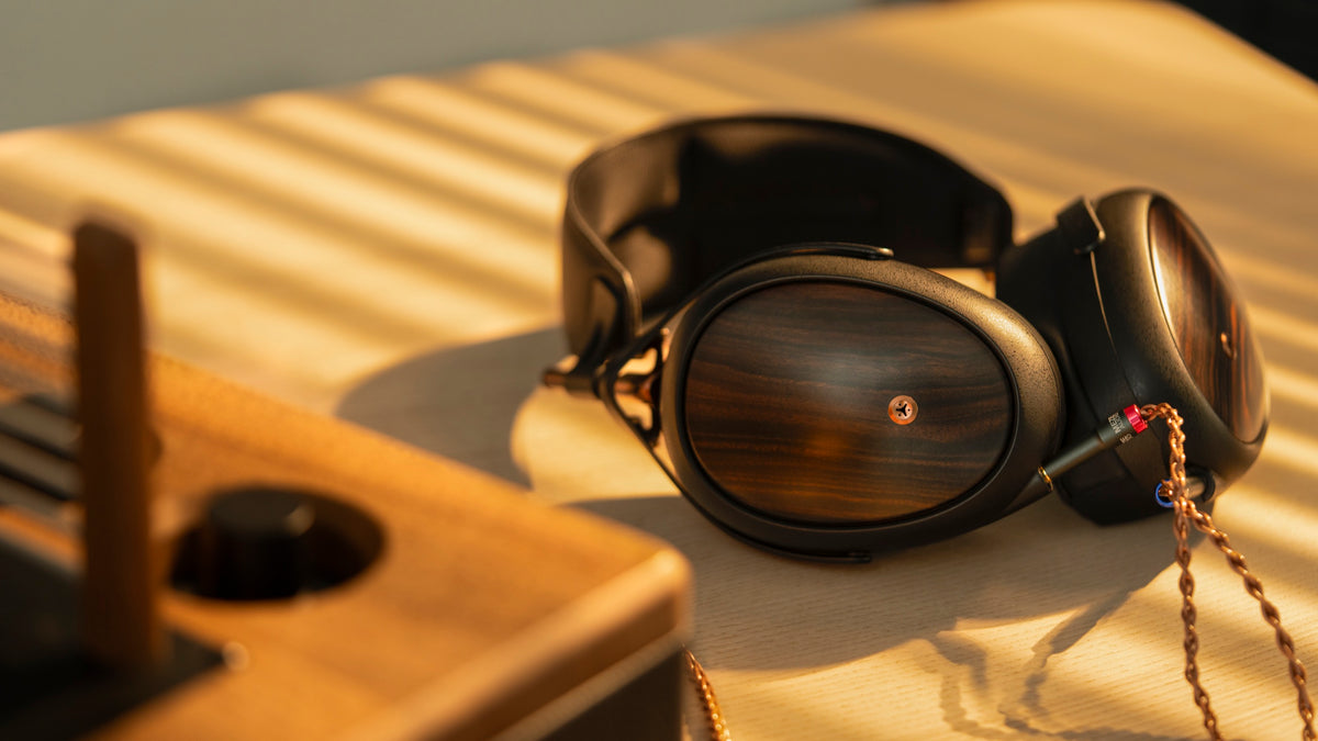 Headphones on a pale wood desk striped with bars of afternoon sun, the cable coiled beside them