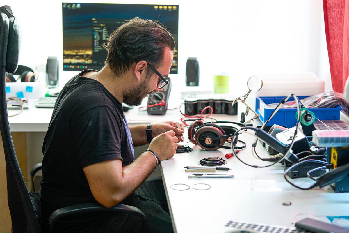 An engineer at a white workbench in Meze's workshop in Baia Mare, working on a headphone among parts, tools and a magnifier