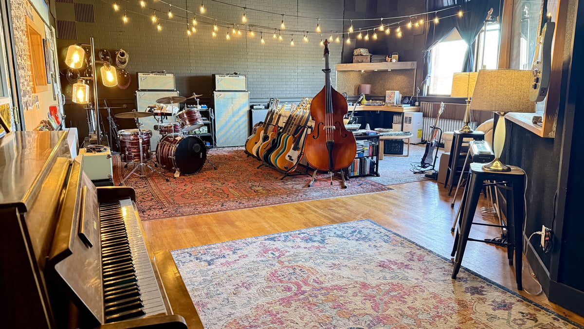 The listening room at Free River Studios in Livingston, with an upright piano, a drum kit, Fender amplifiers, a rack of guitars and an upright bass under string lights